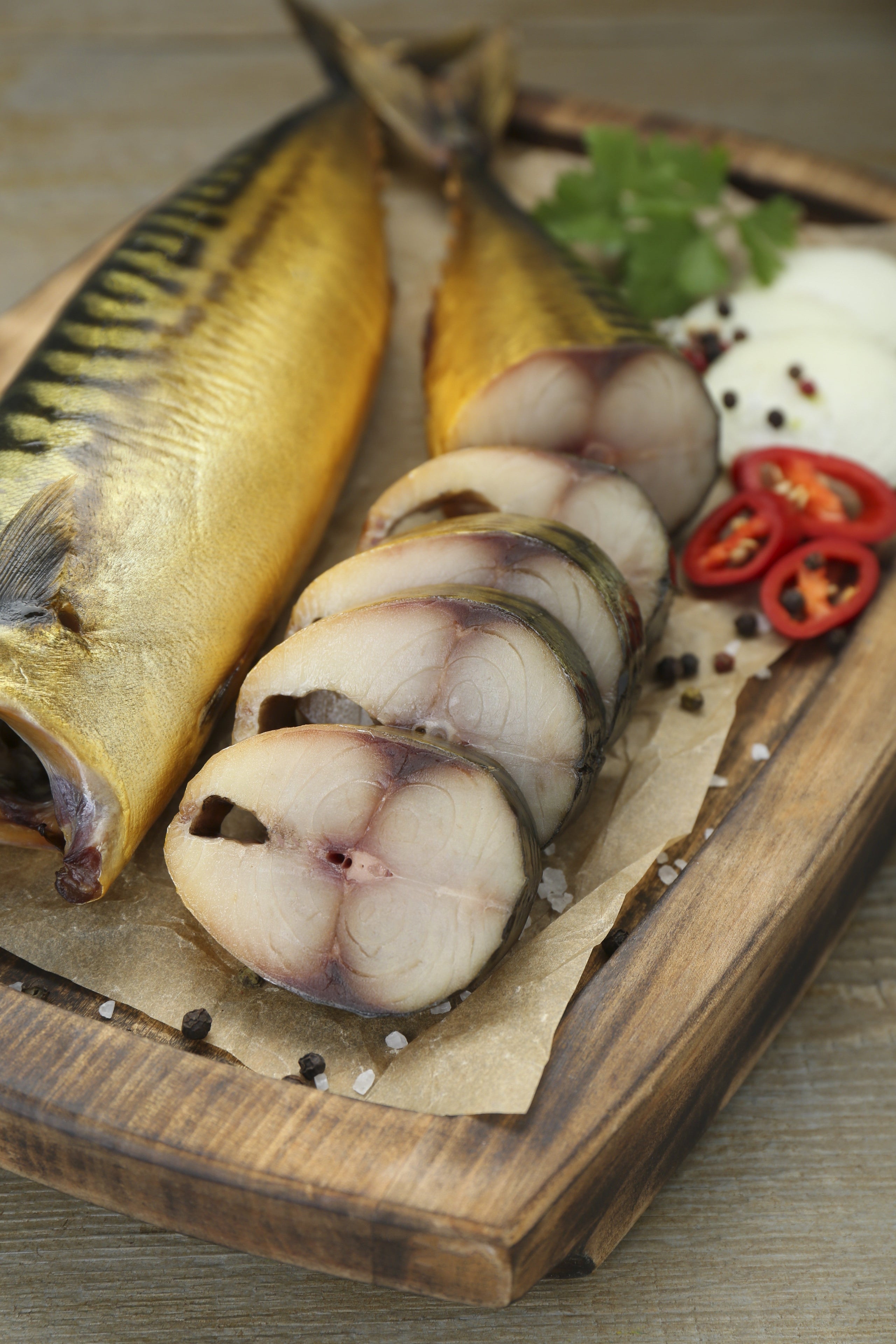 Sliced fish on a wooden cutting board with spices and herbs